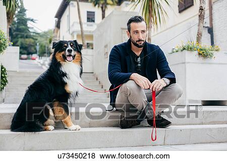 Stock Photo - Mid adult man sitting on stairway with pet dog in city square. Fotosearch