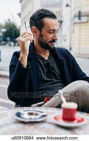 Mid adult man smoking cigarette at sidewalk cafe View Large Photo Image Picture - Mid adult man smoking cigarette at sidewalk cafe. Fotosearch