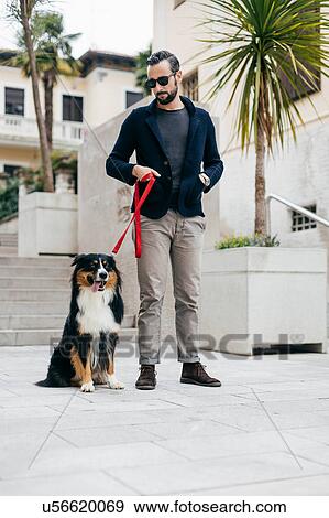 Stock Photo - Mid adult man standing with pet dog in city square. Fotosearch