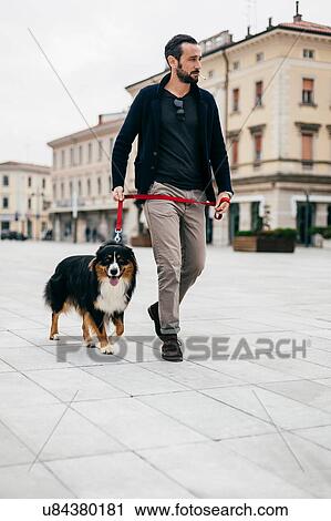 Stock Image - Mid adult man walking dog at city square. Fotosearch