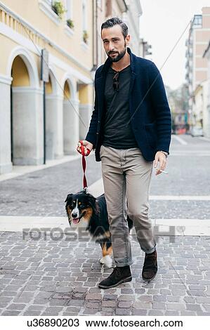 Stock Image - Mid adult man walking his dog in cobbled city street. Fotosearch