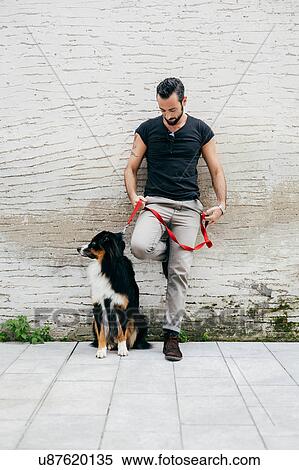 Stock Photography - Mid adult man with dog leaning against wall. Fotosearch