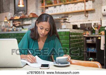 Stock Photography - Mid adult woman doing paperwork at cafe table. Fotosearch