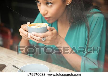 Mid adult woman holding coffee cup looking out of cafe window View Large Photo Image Stock Photo - Mid adult woman holding coffee cup looking out of cafe window. Fotosearch