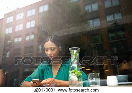 Mid adult woman reading smartphone texts in cafe window seat View Large Photo Image Stock Photo - Mid adult woman reading smartphone texts in cafe window seat. Fotosearch