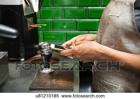 Stock Photography - Mid section of female barista texting on smartphone in cafe kitchen. Fotosearch