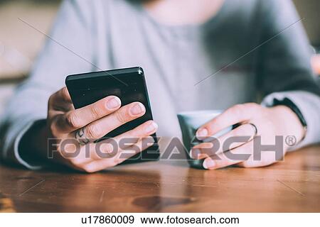 Stock Photo - Mid section of young woman at table holding smartphone and espresso. Fotosearch