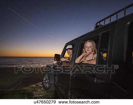 Stock Photo - Mother and daughter (4-5) sitting in car on beach. Fotosearch