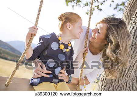Stock Image - Mother with girl (4-5) sitting on swing. Fotosearch