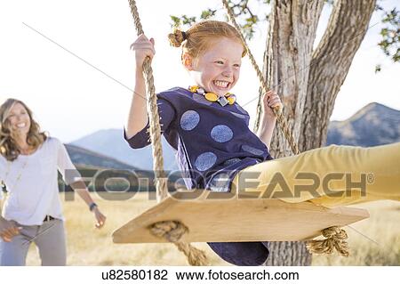 Stock Image - Mother with girl (4-5) sitting on swing. Fotosearch