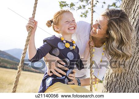 Stock Photograph - Mother with girl (4-5) sitting on swing. Fotosearch
