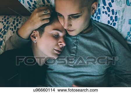 Picture - Overhead view of young lesbian couple lying on bed. Fotosearch