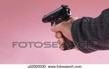 Stock Image - Person holding handgun against a pink background. Fotosearch