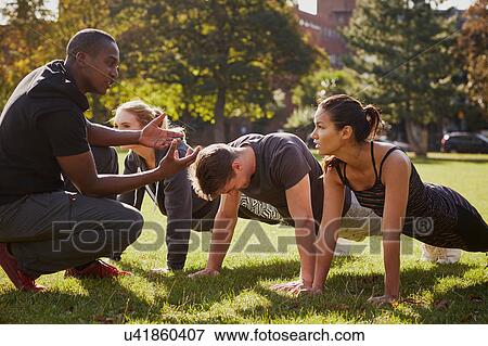 Stock Photo - Personal trainer instructing man and women doing push ups in park. Fotosearch