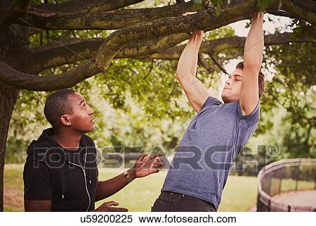Stock Photography - Personal trainer instructing man on pull ups using park tree branch. Fotosearch