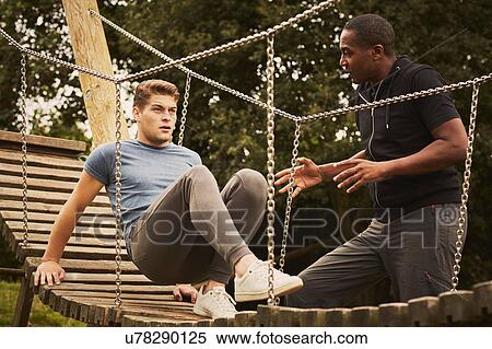 Stock Photography - Personal trainer instructing man training on playground equipment in park. Fotosearch