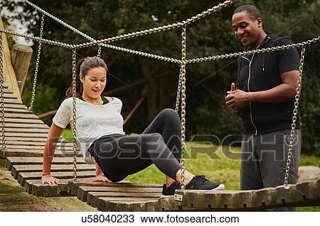 Stock Image - Personal trainer instructing woman training on playground equipment in park. Fotosearch