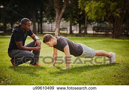 Personal trainer instructing young man doing push ups in park View Large Photo Image Stock Photo - Personal trainer instructing young man doing push ups in park. Fotosearch