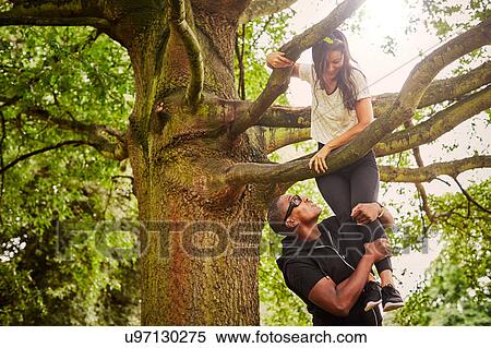 Stock Photography - Personal trainer lifting woman to climb park tree. Fotosearch