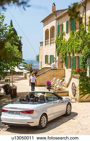 Stock Image - Porter welcoming couple driving convertible to boutique hotel, Majorca, Spain. Fotosearch