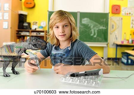 Stock Image - Portrait of boy with hand held computer and 3D model of tyrannosaurus rex. Fotosearch