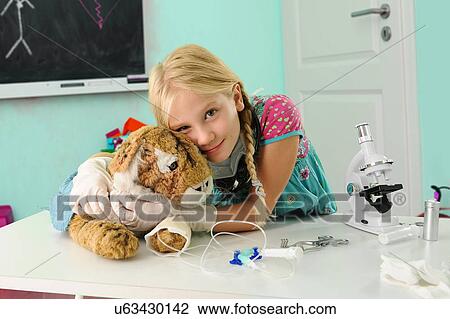 Stock Image - Portrait of girl pretending to be vet hugging toy tiger with intravenous drip. Fotosearch