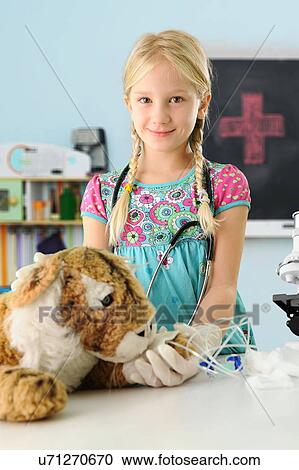 Stock Image - Portrait of girl pretending to be vet to toy tiger with intravenous drip. Fotosearch