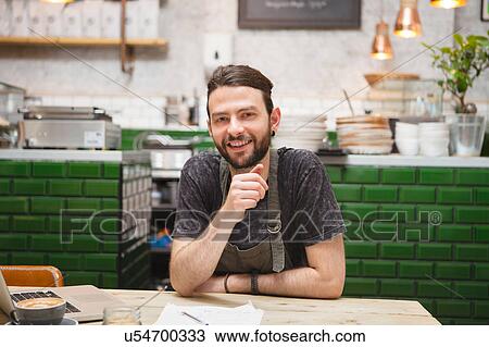 Stock Image - Portrait of male cafe owner doing paperwork at table. Fotosearch