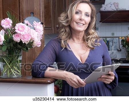 Picture - Portrait of mature female food blogger using digital tablet in traditional Italian kitchen. Fotosearch
