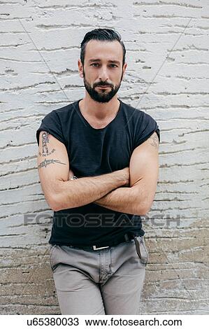 Stock Image - Portrait of mid adult man with arms folded leaning against wall. Fotosearch