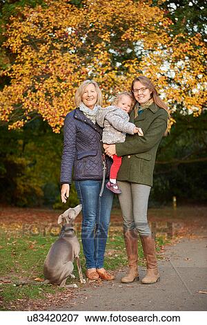 Stock Photo - Portrait of senior woman, daughter, granddaughter and dog in autumn park. Fotosearch