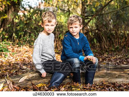 Stock Image - Portrait of twin boys, outdoors, sitting on log in autumn. Fotosearch