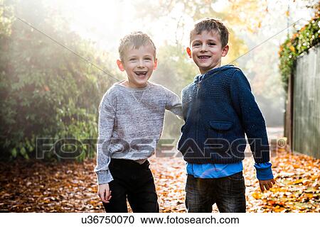 Stock Image - Portrait of twin boys, outdoors, surrounded by autumn leaves, laughing. Fotosearch