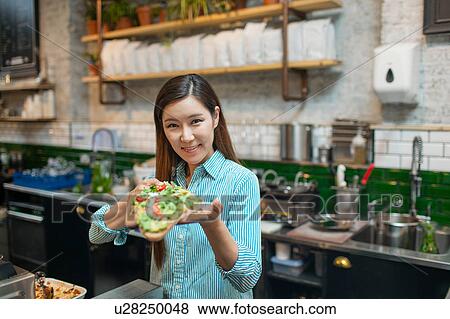 Stock Photo - Portrait of waitress holding open sandwich in cafe. Fotosearch