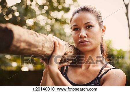 Stock Image - Portrait of woman training, lifting tree trunk on shoulder in park. Fotosearch