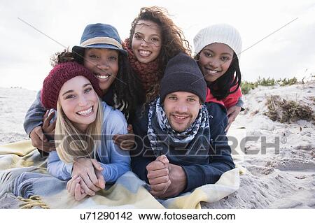 Stock Image - Portrait of young adult friends lying on top of each other on beach, Western Cape, South Africa. Fotosearch
