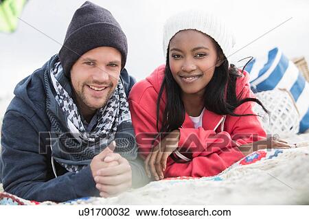 Stock Image - Portrait of young couple lying on picnic blanket at beach, Western Cape, South Africa. Fotosearch