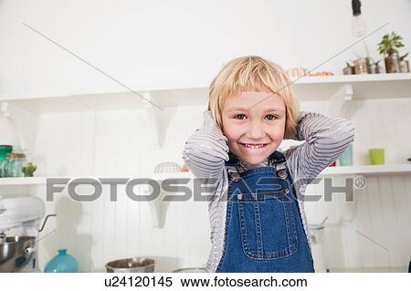 Stock Photography - Portrait of young girl in kitchen, hands behind head, smiling. Fotosearch