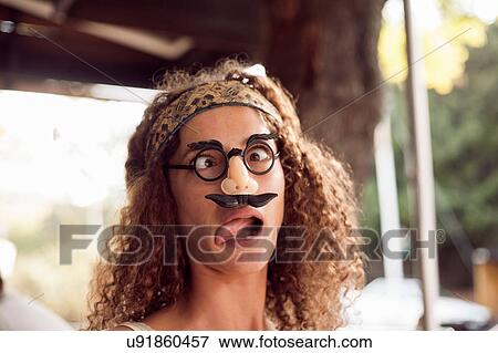 Stock Photo - Portrait of young woman pulling a face wearing false mustache and spectacles. Fotosearch