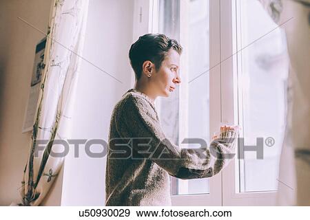 Portrait of young woman staring through window at home View Large Photo Image Stock Photo - Portrait of young woman staring through window at home. Fotosearch