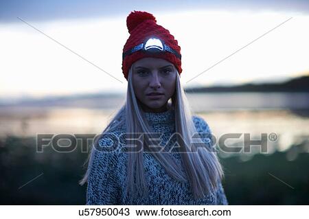 Stock Image - Portrait of young woman with head torch by sea at dusk. Fotosearch