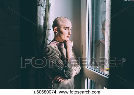 Portrait of young woman with shaved head gazing through window View Large Photo Image Picture - Portrait of young woman with shaved head gazing through window. Fotosearch