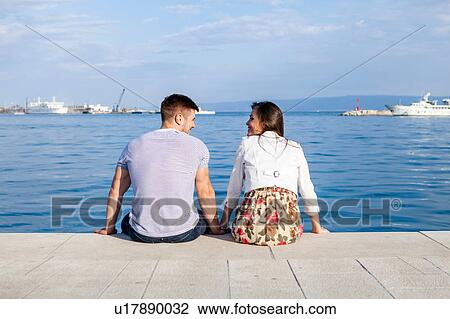 Stock Image - Rear view of couple sitting on harbour, Split, Dalmatia, Croatia. Fotosearch