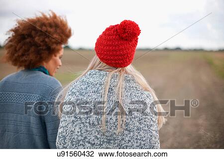 Stock Image - Rear view of two young women strolling in field. Fotosearch