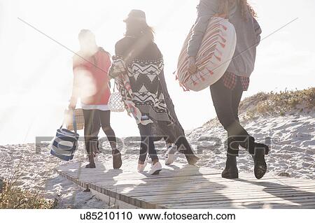 Stock Image - Rear view of young adult friends strolling on sunlit boardwalk at beach, Western Cape, South Africa. Fotosearch