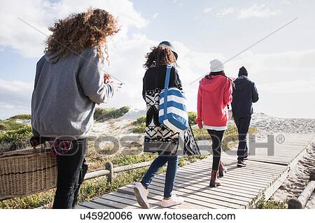Rear view of young adult friends strolling along beach boardwalk reading smartphones, Western Cape, South Africa View Large Photo Image Stock Photograph - Rear view of young adult friends strolling along beach boardwalk reading smartphones, Western Cape, South Africa. Fotosearch