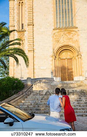 Stock Photo - Rear view of young couple with convertible looking at map, Calvia, Majorca, Spain. Fotosearch
