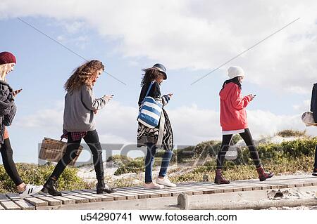 Row of young adult friends strolling along beach boardwalk reading smartphones, Western Cape, South Africa View Large Photo Image Stock Image - Row of young adult friends strolling along beach boardwalk reading smartphones, Western Cape, South Africa. Fotosearch