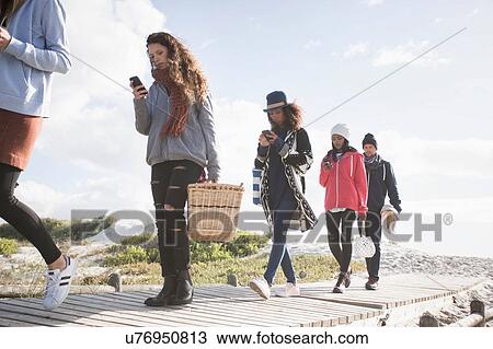Row of young adult friends strolling along beach boardwalk reading smartphones, Western Cape, South Africa View Large Photo Image Stock Image - Row of young adult friends strolling along beach boardwalk reading smartphones, Western Cape, South Africa. Fotosearch