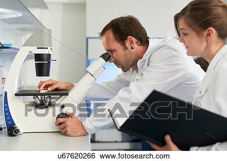 Stock Photograph - Scientist in laboratory looking through microscope. Fotosearch